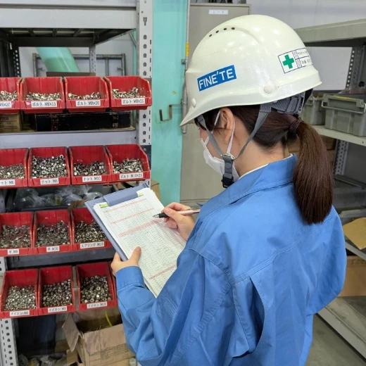 ヘルメットを着用し、部品棚の前で在庫を確認する女性スタッフ