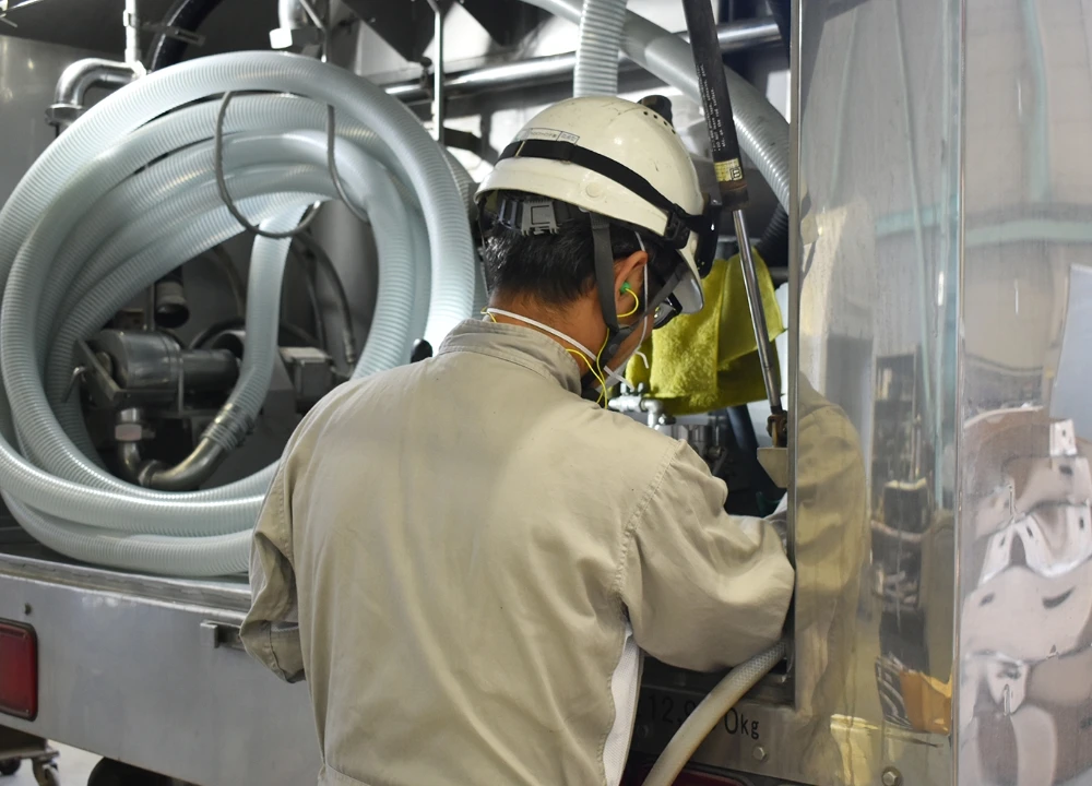 タンクローリーの背面にある配管やホースの点検・メンテナンスを丁寧に行う技術者の後ろ姿