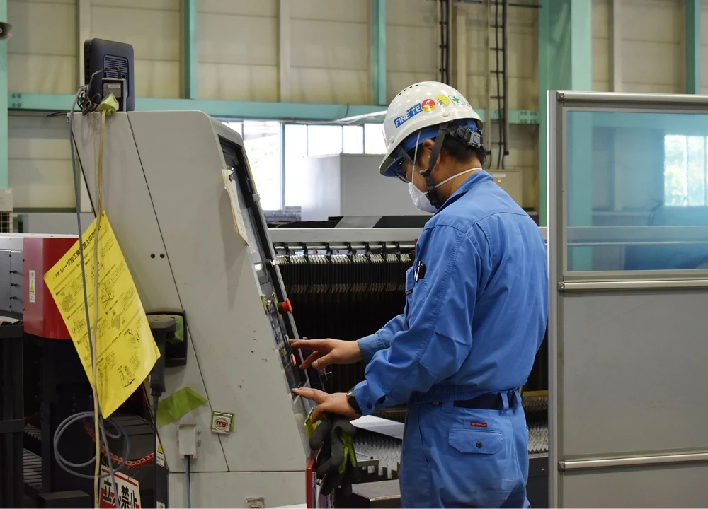 工場内でレーザー加工機などの工作機械を操作する、ヘルメットと作業服を着用した技術スタッフ