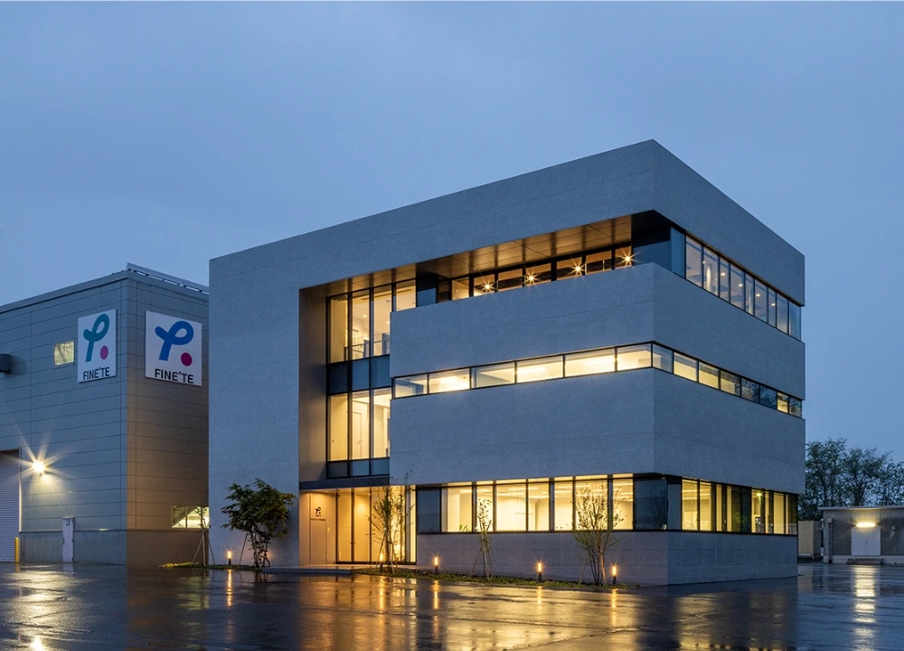 夕暮れ時にライトアップされたFINE'TEのモダンなオフィスビルと工場の外観