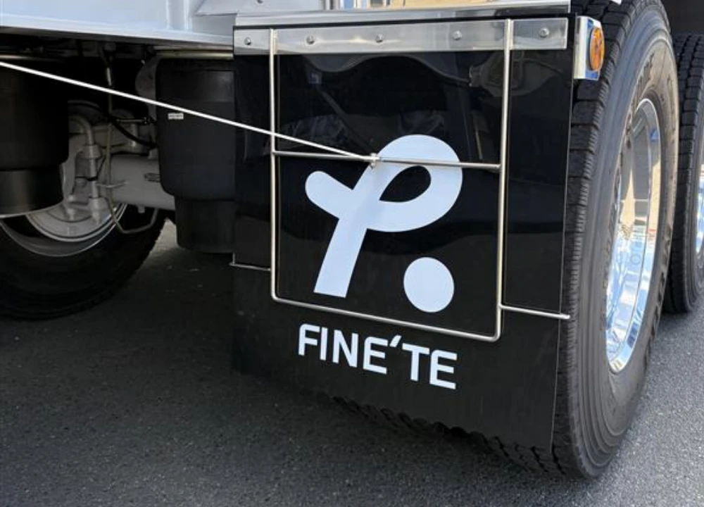 トラックのタイヤ後部に取り付けられた、FINE'TEのブランドロゴと社名がデザインされた黒いマッドガード（泥除け）