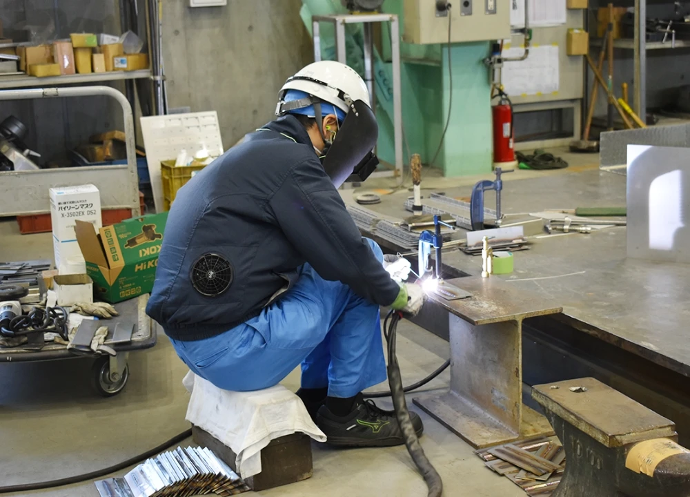工場内で火花を散らしながら精密な溶接作業を行う作業員。空調服を着用し、安全に配慮した作業風景