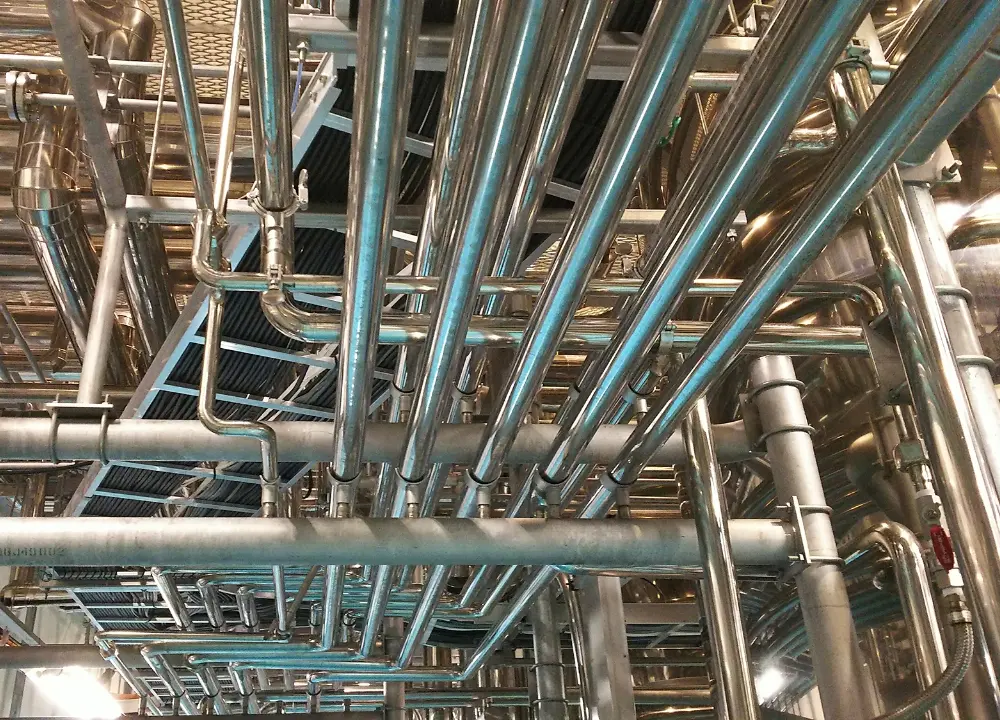 工場内に整然と張り巡らされた、美しく輝くステンレス製のサニタリー配管のクローズアップ