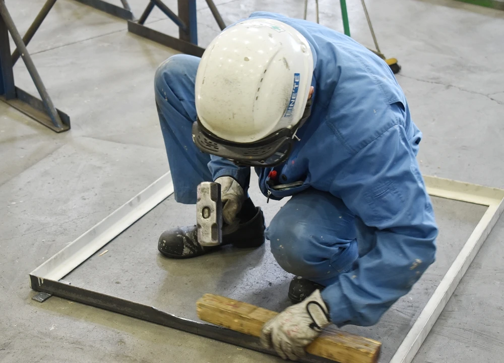 作業服とヘルメットを着用し、ハンマーを使って金属パーツの精密な手作業による調整を行う熟練工