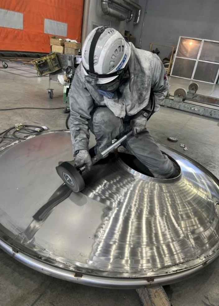 工場内で金属製タンク部品を研磨する作業員