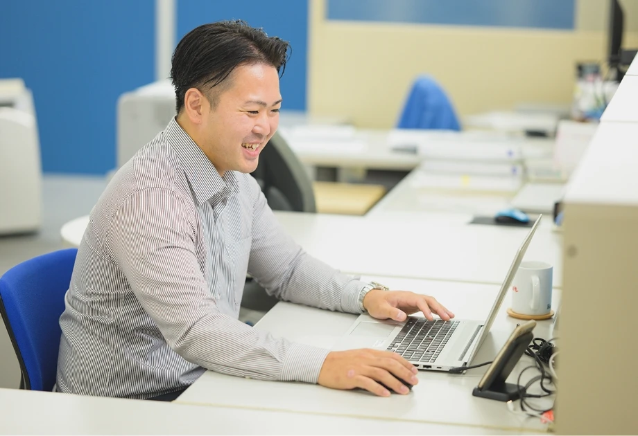 デスクで笑顔でノートパソコンを操作する男性社員
