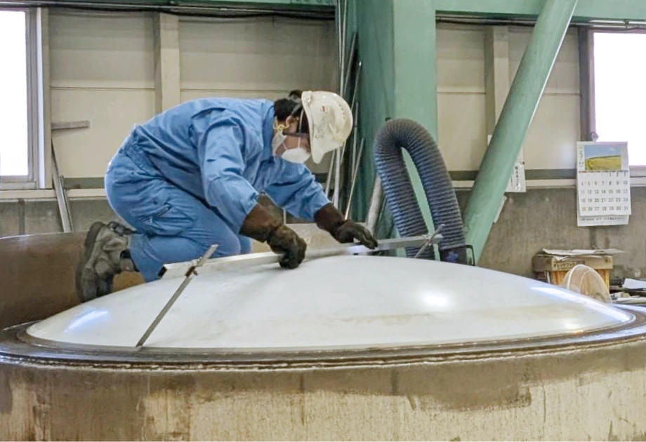 工場内で大型製品の表面を丁寧に測定・確認する作業員