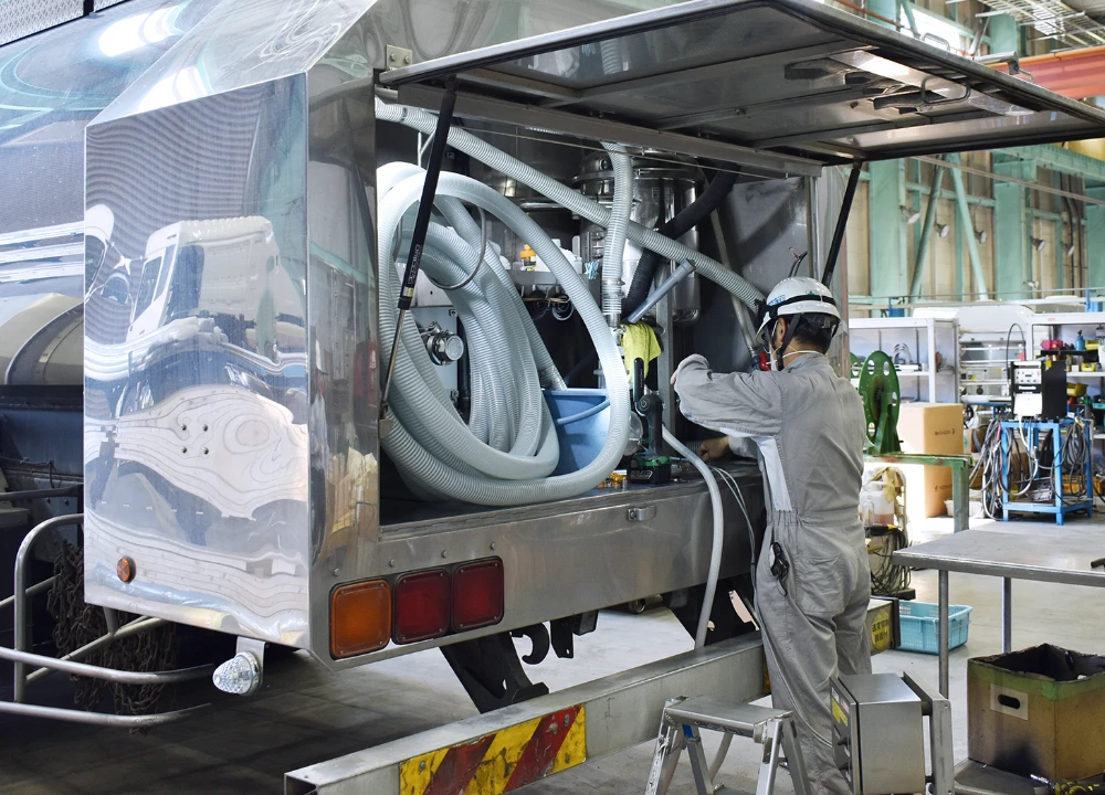 大型タンクローリーの背面にあるハッチを開け、内部のホースや配管設備を点検・整備する作業員