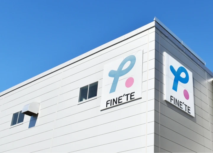 青空の下にあるFINE'TEのロゴが付いた白い工場の外観。