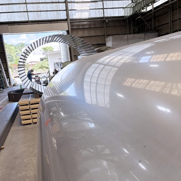 工場内で加工中の大型金属部品。鏡面仕上げの曲面と円形金属フレーム。