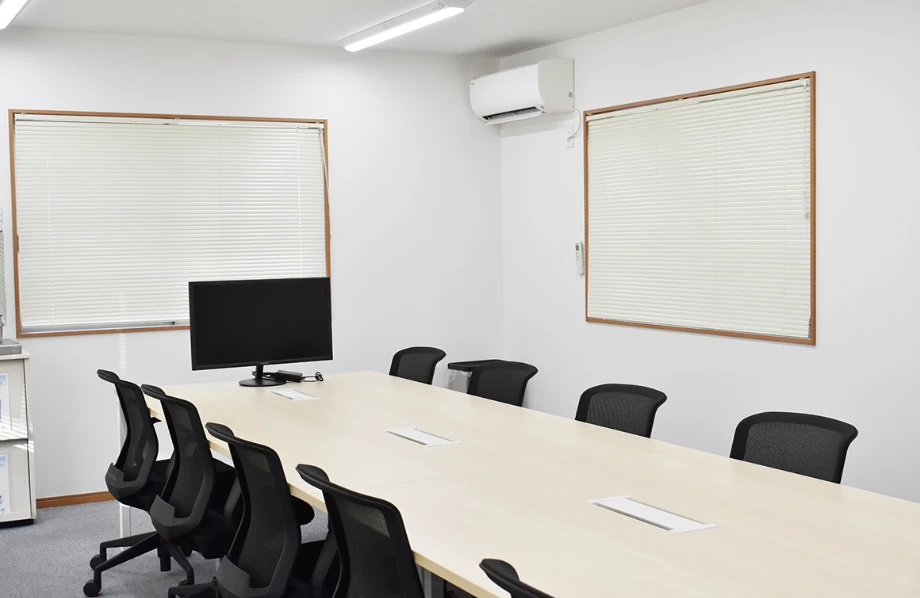 会議室のデスクと椅子、モニター付きのシンプルなオフィス空間。