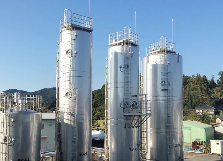工業用ステンレスタンクの外観、青空と山背景の製造施設。