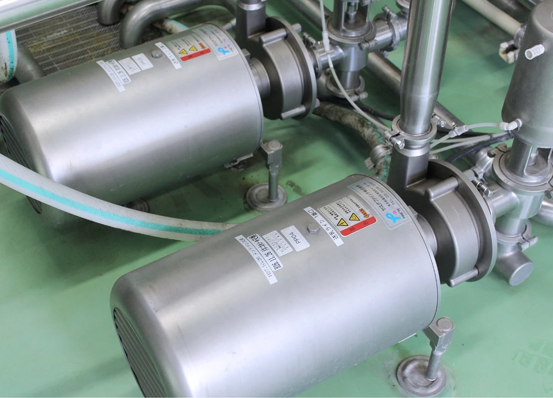 工場の配管に接続されたステンレス製のポンプ機械装置。