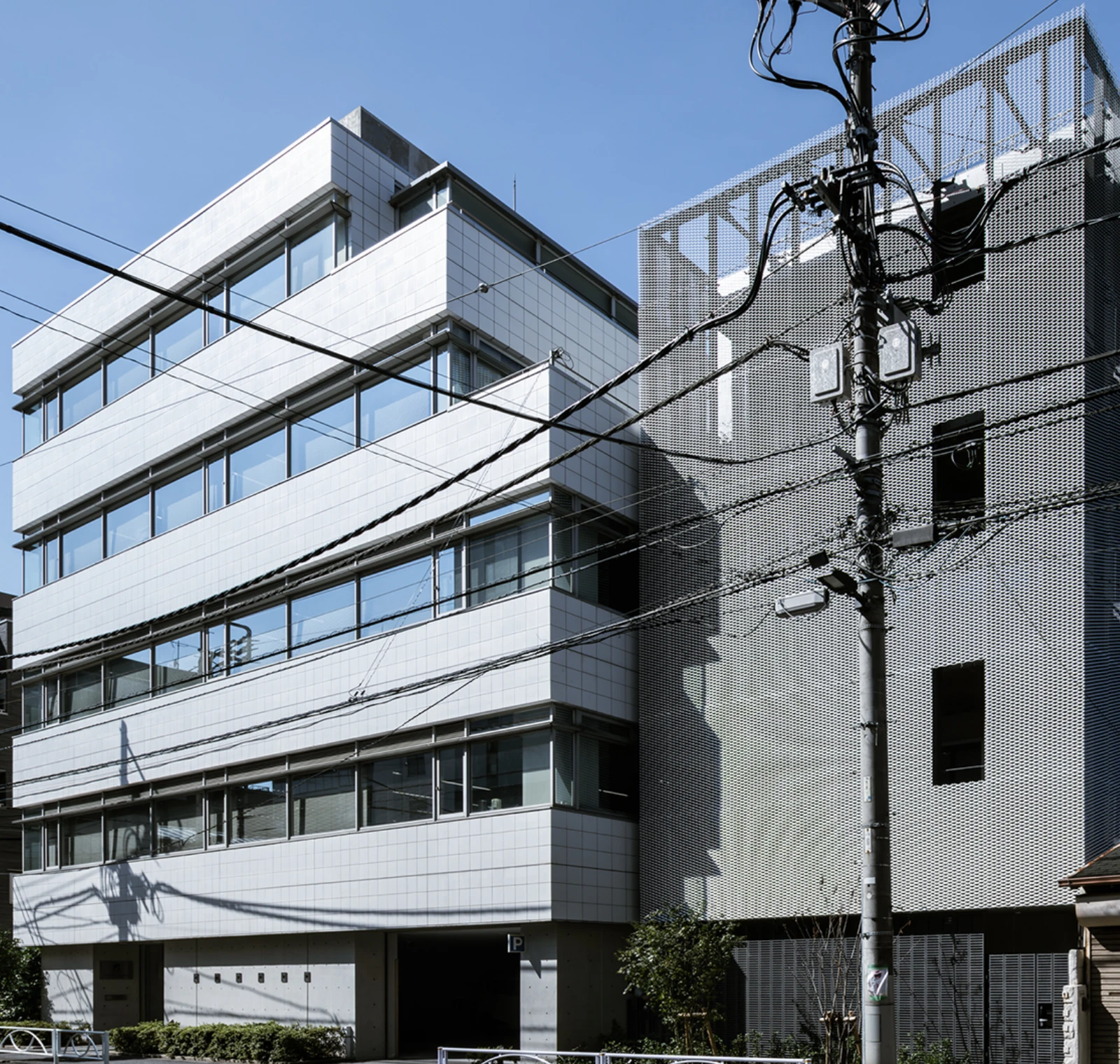 白いタイルの現代的なオフィスビルとメッシュ外壁の建物、青空と電線が見える街並み